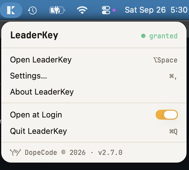 The LeaderKey menu-bar panel open under its K icon: the LeaderKey name with granted in green, then Open LeaderKey with Option-Space, Settings with Command-comma, About LeaderKey, an amber Open at Login switch, Quit LeaderKey with Command-Q, and DopeCode © 2026 · v2.7.0 at the foot.